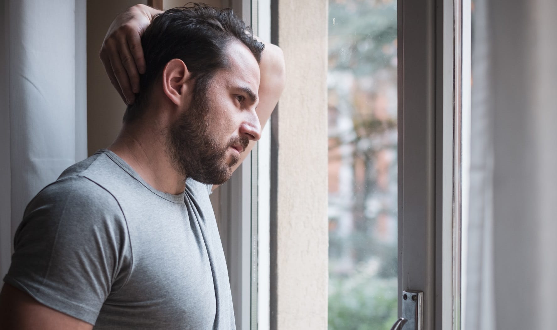 A man looking pensively out of a window at home